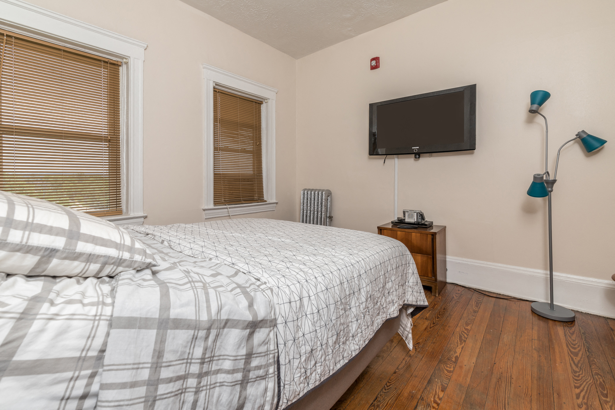 A bedroom with a bed, a television, and a window with blinds.
